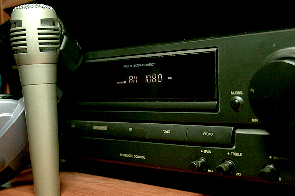 A silver microphone leaning against a black radio, set to AM 1080, sitting on a wooden desktop.