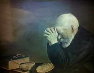 An old man seated and praying at a table with scripture, bread, and a bowl sitting on the tabl.