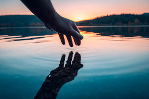A hand touching water at sunset.