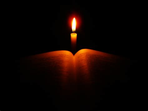 Scripture backlit by a single candle on a jet black background.