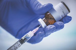 A blue gloved hand filling a syringe from a vial.