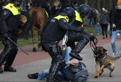 Three police beating a man on the ground with his arms covering his head.