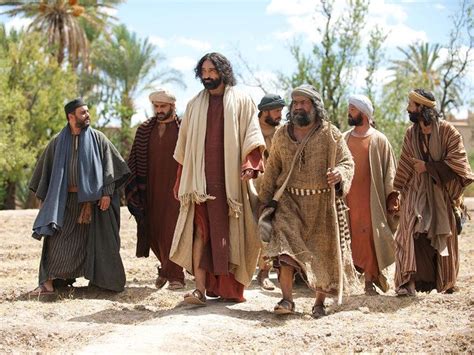 A group of middle eastern men walking in the sand outside with trees and the walls of a city in the background.